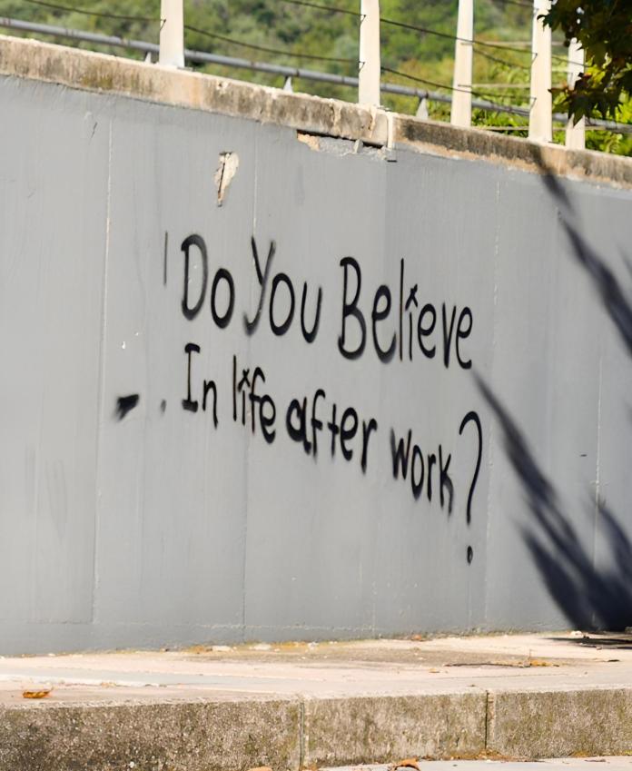 Black graffiti asking "Do you believe in life after work?" spray-painted on a grey wall.