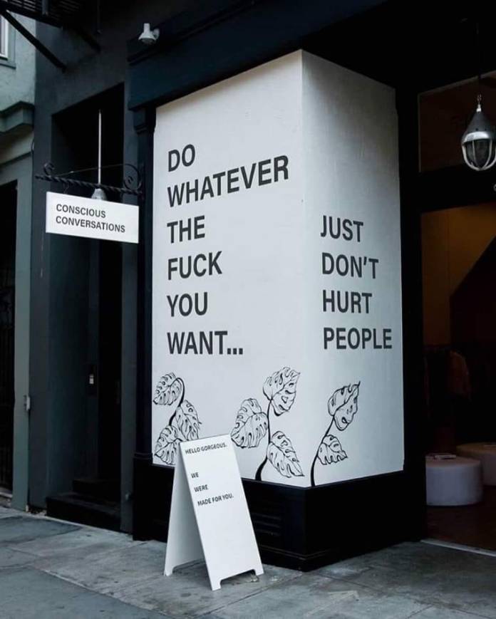 Street art reading "Do whatever the fuck you want... just don't hurt people" painted on a white building corner.