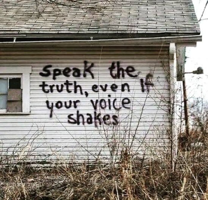 Graffiti saying "Speak the truth, even if your voice shakes" painted on a white abandoned building wall.