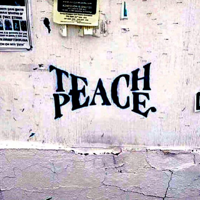 Black painted graffiti cleverly combining the words "Teach" and "Peace" on an old white wall.
