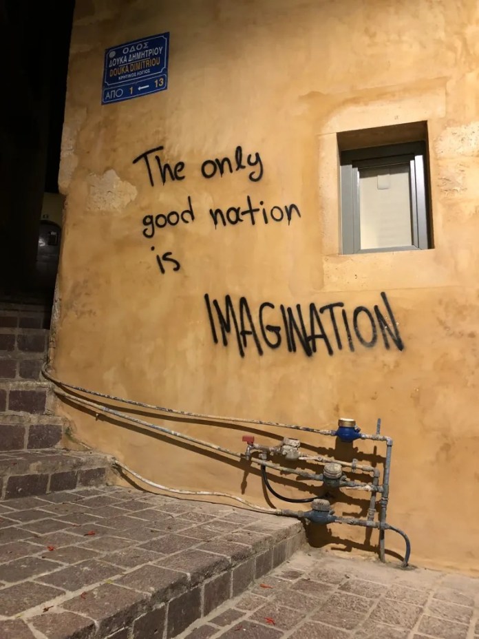 Graffiti reading "The only good nation is imagination" sprayed in black letters on a yellow wall in an alley.