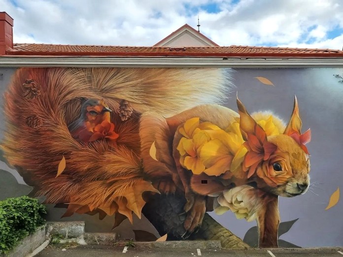 A wall-sized mural of a red squirrel decorated with yellow-orange flowers, with a robin tucked into its curled tail, set on a gray wall in Sweden.