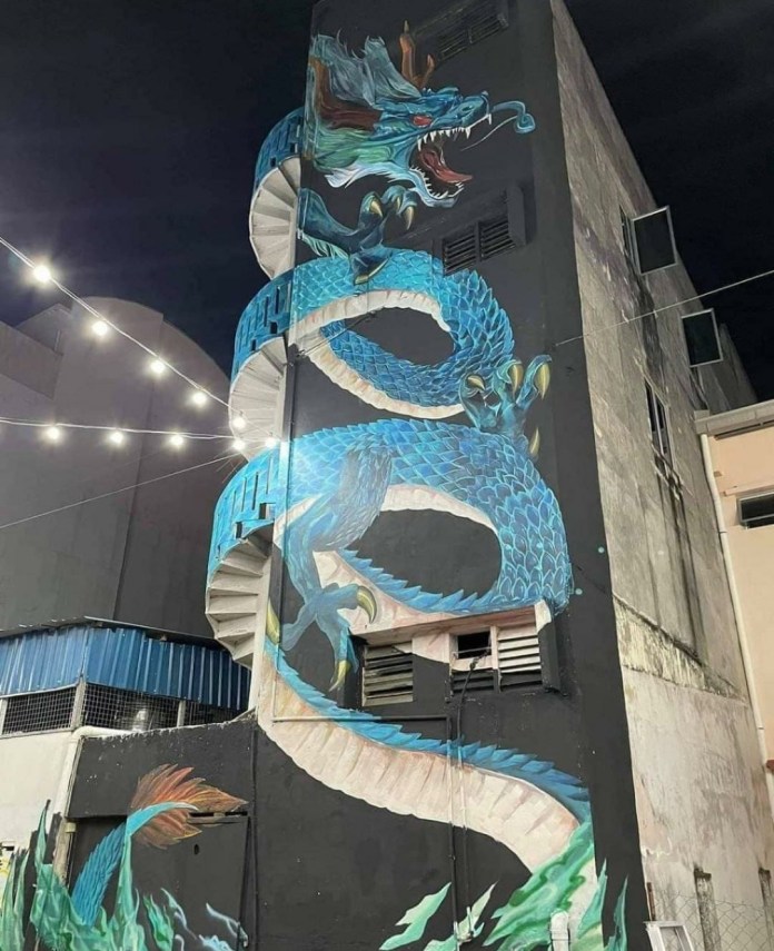 A massive blue-green dragon mural wraps around a three-story black building in Malaysia, using a spiral staircase as part of the body to simulate movement.