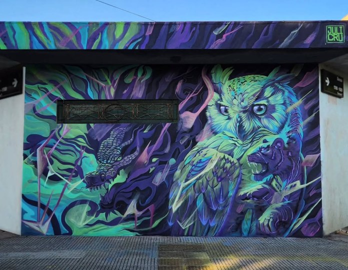 A neon mural in Buenos Aires shows a luminous owl and a coiled dragon against swirling purple, green, and blue abstract backgrounds.