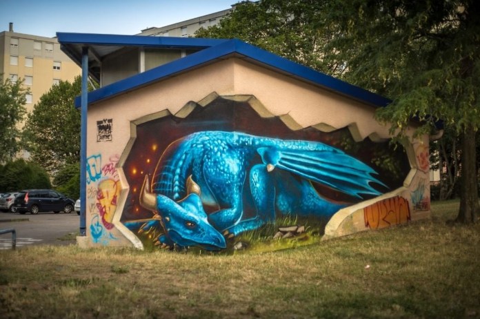 A green dragon mural by Braga Last1 in Le Pont-de-Claix, France, painted within the empty brick holes of a red brick wall, with its curled tail and head emerging toward a nearby painted mouse on the concrete.