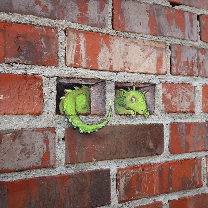 A cartoon-style green dragon lies on its back drawn on the sidewalk with a mouse nearby, surrounded by real autumn leaves in Michigan.