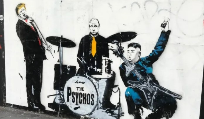 Satirical street art by Loretto from 2018 in Shoreditch, London, UK, depicting a mock band called 'The Psychos.' The mural features caricatures of world leaders: Donald Trump on vocals, Vladimir Putin on drums, and Kim Jong-un playing a guitar. Trump leans into the microphone, Putin sits stoically with a yellow tie, and Kim strikes a rockstar pose with a peace sign and an electric guitar. The band's name is boldly painted on the drum kit, adding a comedic yet politically charged edge to the artwork. Graffiti tags and a worn urban wall form the backdrop.