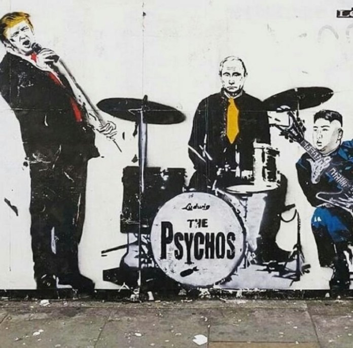 Satirical street art by Loretto from 2018 in Shoreditch, London, UK, depicting a mock band called 'The Psychos.' The mural features caricatures of world leaders: Donald Trump on vocals, Vladimir Putin on drums, and Kim Jong-un playing a guitar. Trump leans into the microphone, Putin sits stoically with a yellow tie, and Kim strikes a rockstar pose with a peace sign and an electric guitar. The band's name is boldly painted on the drum kit, adding a comedic yet politically charged edge to the artwork. Graffiti tags and a worn urban wall form the backdrop.