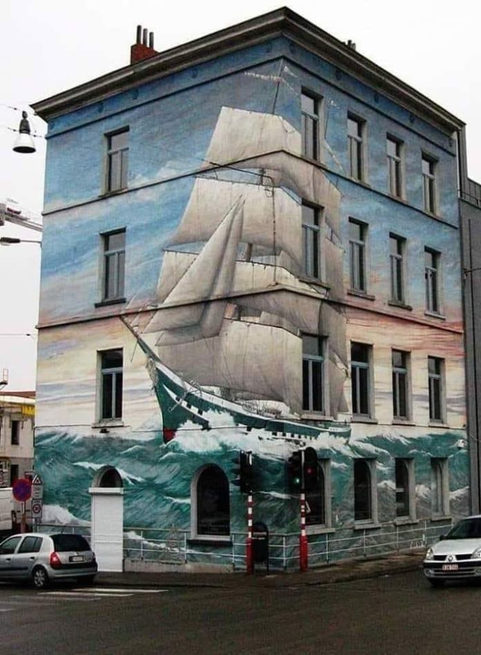 Large-scale mural covering a building in Brussels depicting a tall ship navigating through waves, painted to appear three-dimensional with the building’s shape.