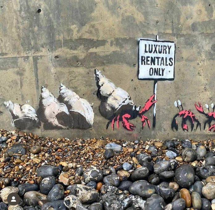 Banksy’s mural on a sea wall showing a line of crabs and hermit crabs facing a “Luxury Rentals Only” sign. One large crab excludes others from the available shell homes.