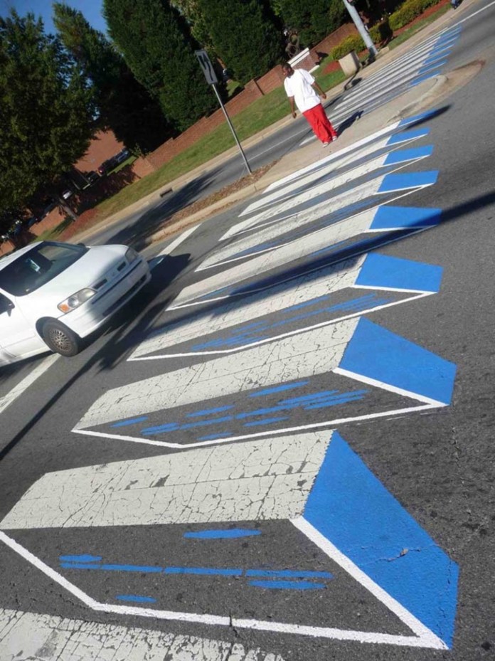 Roadsworth's street art illustrating a domino effect with 3D blocks on a pedestrian crosswalk.