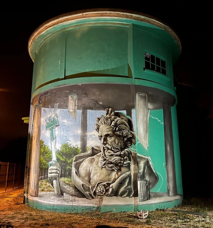 This nighttime image captures the stunning anamorphic mural of Poseidon by Braga Last One in Torreilles, France, for Festival Les Billes S'agitent. Illuminated by soft light, the mural takes on a dramatic tone, emphasizing the intricate details of the ancient Greek deity's figure, his trident, and the illusion of crumbling pillars. The shadows and lighting add depth, making the artwork appear even more lifelike and dynamic under the night sky.
