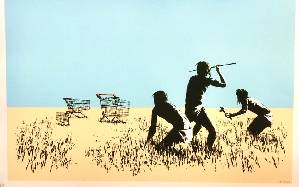 Banksy’s artwork Trolley Hunters, a satirical piece depicting three hunters crouching in a savanna-like landscape, aiming their primitive weapons at two shopping carts. The minimalist background of a clear blue sky and sandy terrain emphasizes the absurdity of the scene, critiquing modern consumer culture and its misplaced priorities.