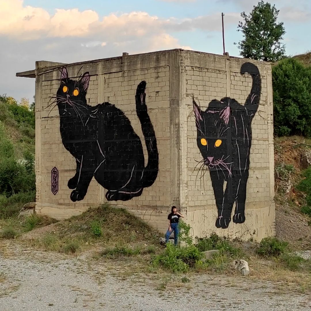 A striking street art mural of a black cat with green eyes by the graffiti crew 3MK in Ptolemaida, Greece.