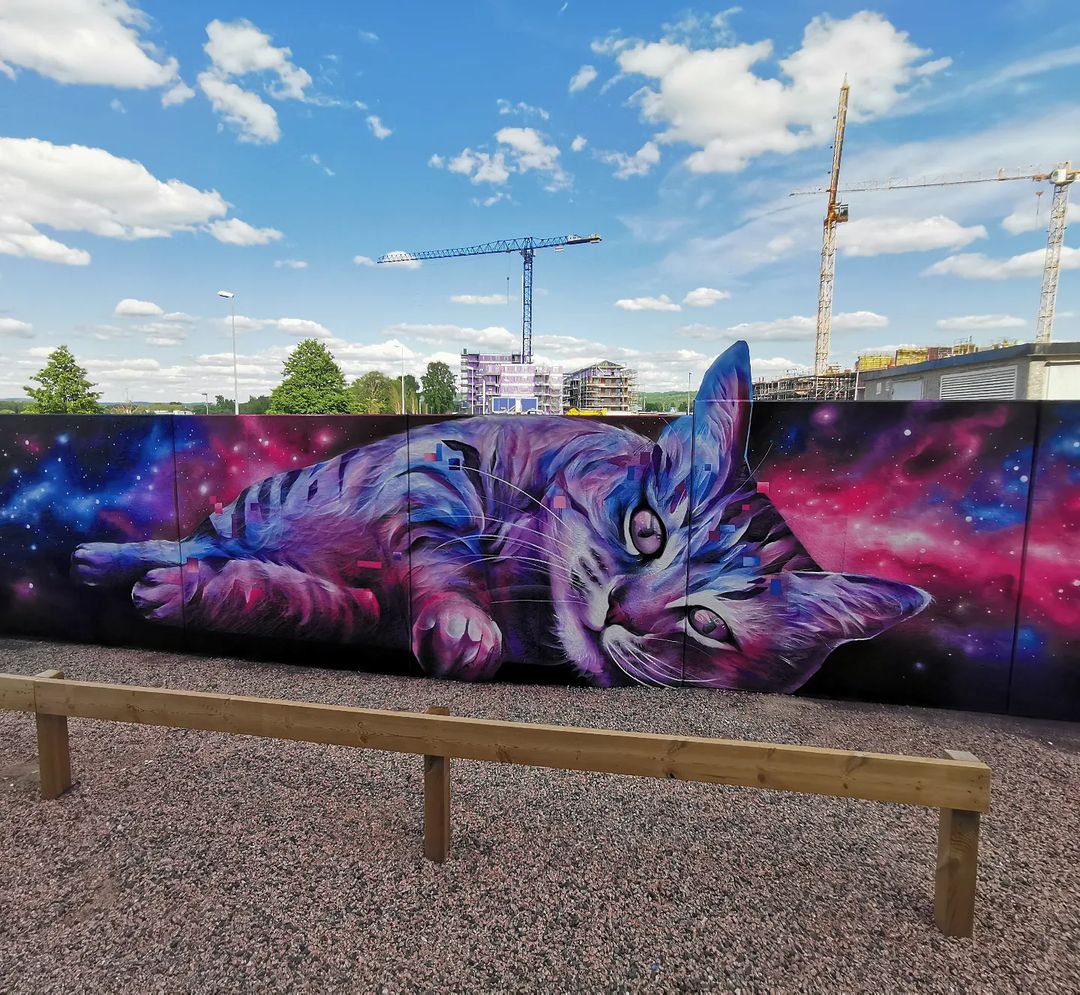 A dreamy street art mural of a cute cat playing with a glowing star by artist Sagie in Jönköping, Sweden.