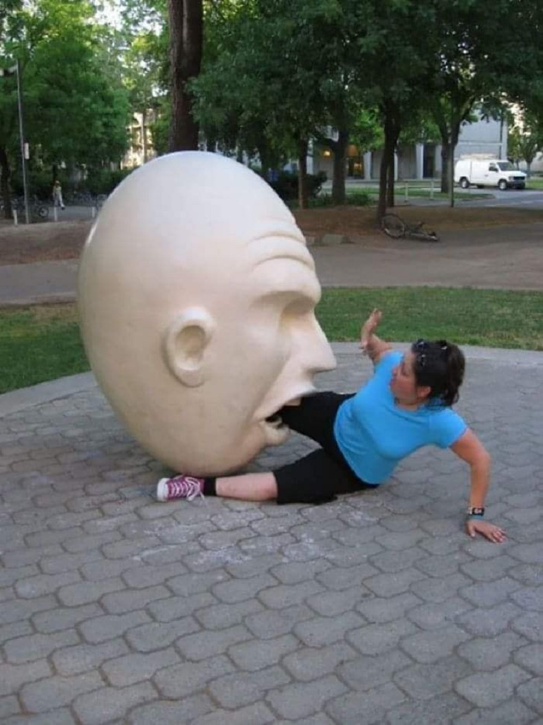 A visitor poses face-to-face with the Yin & Yang egghead street art sculpture by Robert Arneson in Davis, USA. A fun 3D illusion in public graffiti culture.