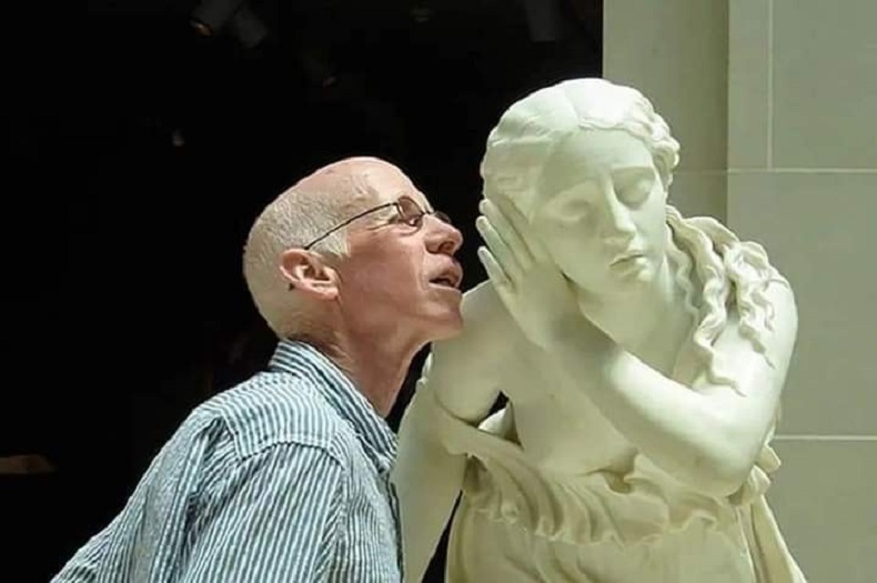 Man playfully whispers a secret to a classical marble bust statue. A funny street art and 3D illusion interaction bridging history and public graffiti.