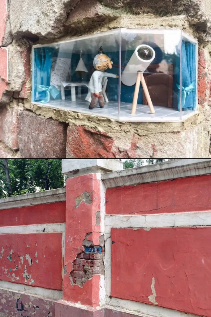 Miniature room built inside a hole in a red brick wall with a tiny man using a telescope