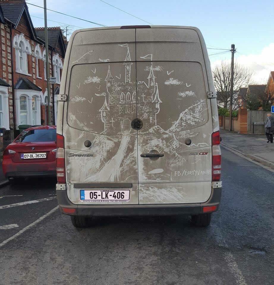 A detailed castle with towers and flags scratched into the dust on the back of a van