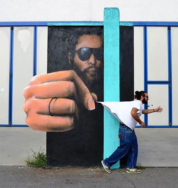 Optical illusion mural by Cosimo CHEONE Caiffa in Italy: a painted man in sunglasses reaches out from a wall and appears to pinch the shirt of a passerby.