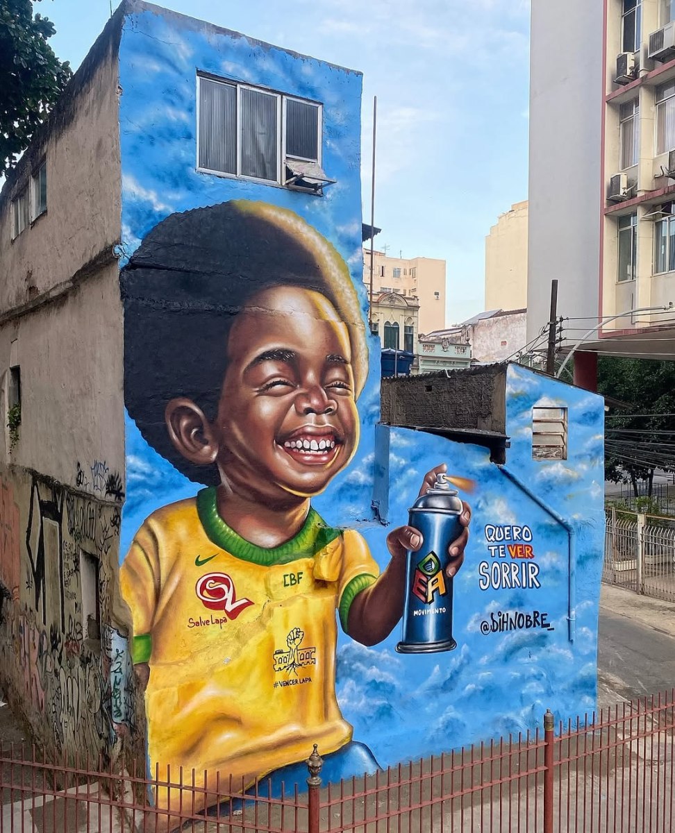 A mural by Diego Nobre in Rio de Janeiro, Brazil, showing a smiling child in a yellow Brazil football shirt holding a spray can against a blue sky background.