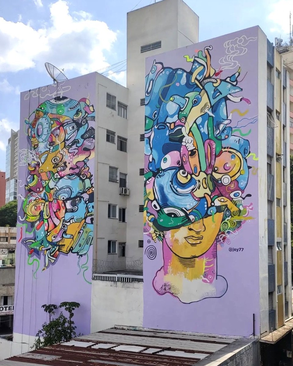 A tall mural by Jey77 in São Paulo, Brazil, showing abstract colorful faces and shapes painted across two high building walls.