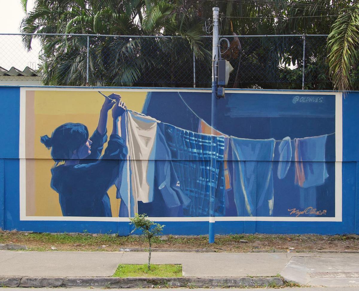 Women of the Favela by Megan Oldhues in Mongaguá, Brazil, showing a blue-toned figure hanging laundry on a clothesline across a wall.