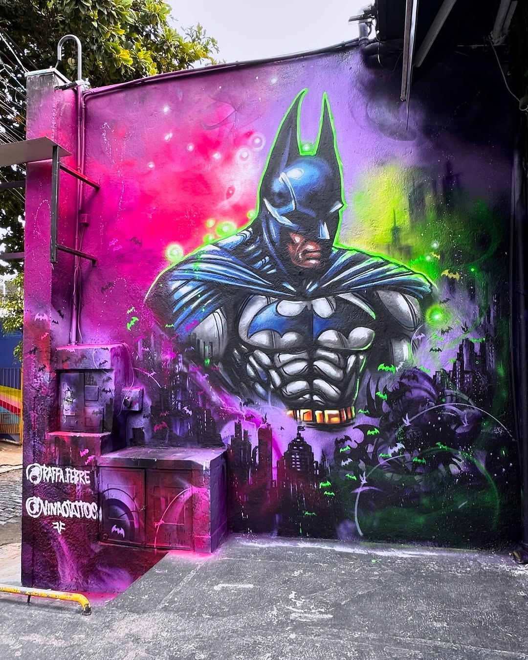 Batman by Raffa.Febre and Vinao in São Paulo, Brazil, showing a masked superhero figure above a purple and green cityscape.