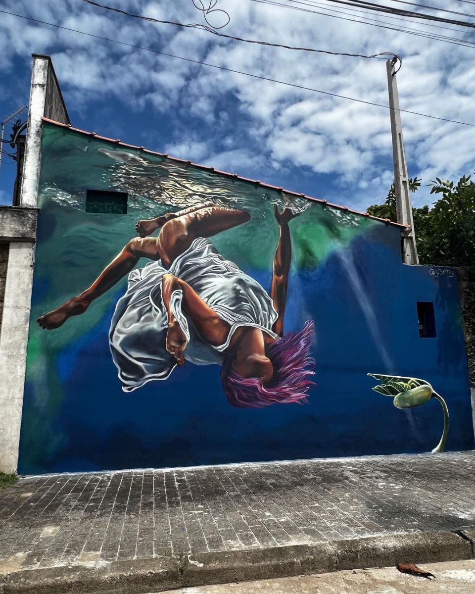 Immersion by Jennifer Erny in Peruíbe, São Paulo, Brazil, showing a floating figure underwater beside a small plant against a deep blue wall.