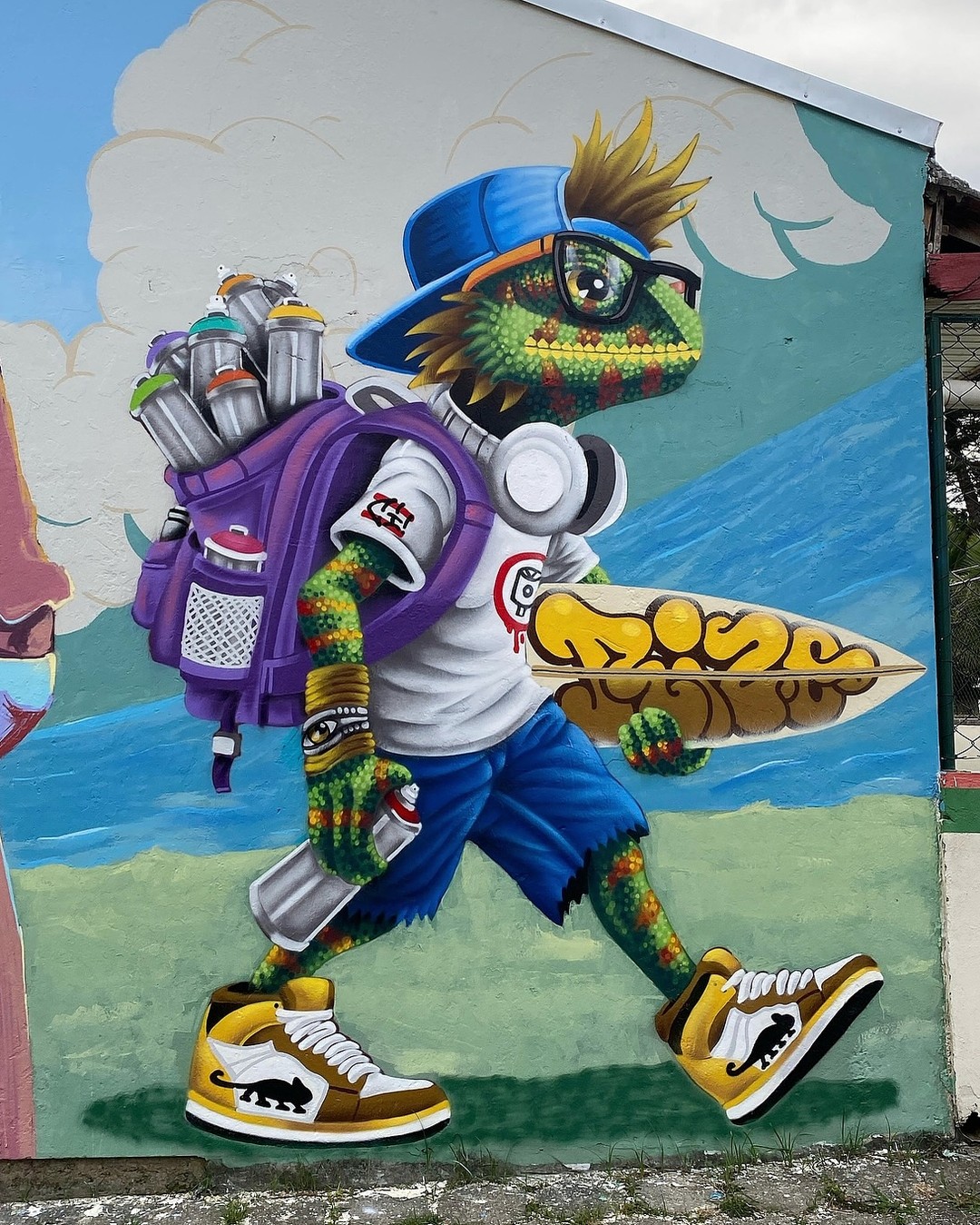 Mural by Rodrigo Rizo in Campeche, Brazil showing a graffiti-style anthropomorphic gecko wearing streetwear, a backpack full of spray paint, and carrying a surfboard, painted with bright, comic-like textures and shading.