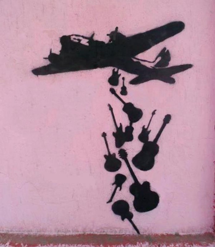 Stencil street art of a plane dropping guitars instead of bombs (Make Music Not War).