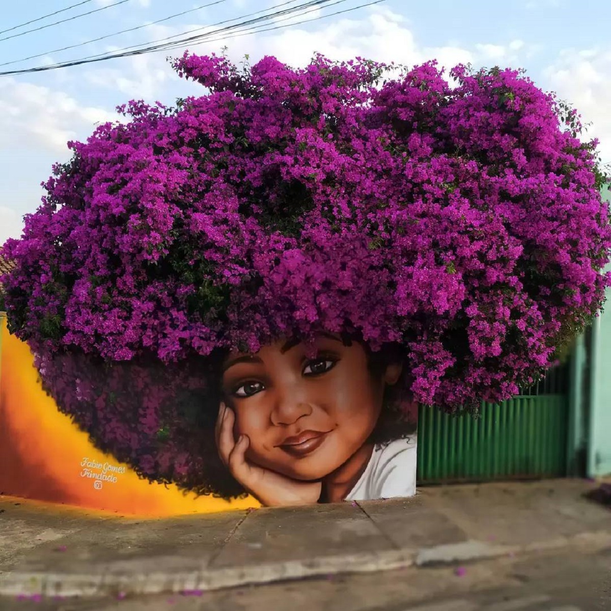 Mural of a smiling girl with her cheek in her hand, placed under a flowering bougainvillea bush that creates the illusion of natural hair in full bloom.