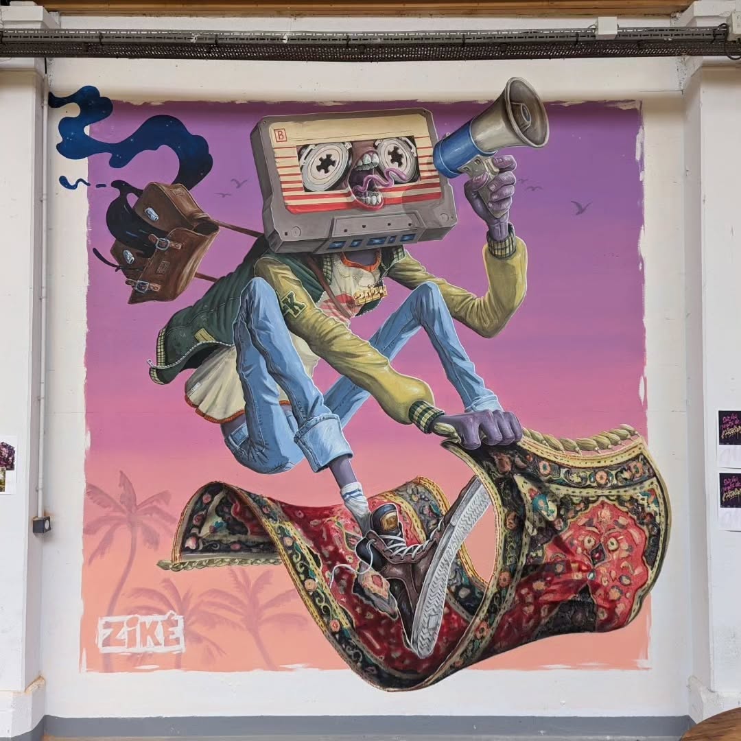 A surreal mural by Zike in Toul, France, featuring a humanoid figure with a cassette tape for a head, complete with spinning reels and a distorted, melted expression. The character, dressed in a vintage streetwear outfit, rides a highly detailed flying carpet, gripping its edges like a skateboarder. In one hand, they hold a megaphone, while a suitcase trails behind, emitting a smoky, dreamlike aura. The background is a soft pink and purple sunset with silhouetted palm trees, giving the piece a retro-futuristic, psychedelic feel.