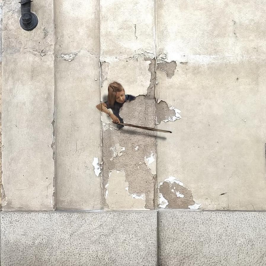 Street art in Milan by Golsa Golchini depicting a girl holding a bow, appearing to play a Double Bass made from the peeling plaster and cracks on the wall. The illusion transforms the broken surface into a poetic urban instrument.