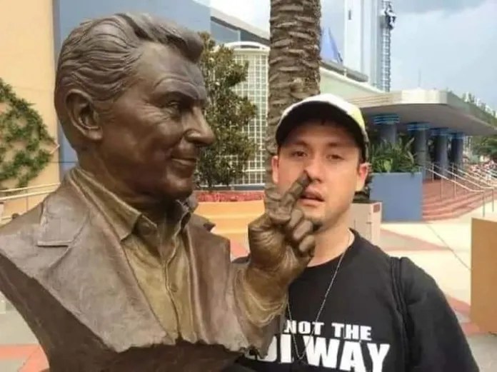 A man positions himself so it looks like the statue’s finger is up his nose.