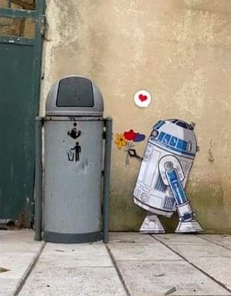 R2-D2 street art by EFIX, showing the droid offering a small bouquet to a real gray trash can with a red heart painted on the wall above.