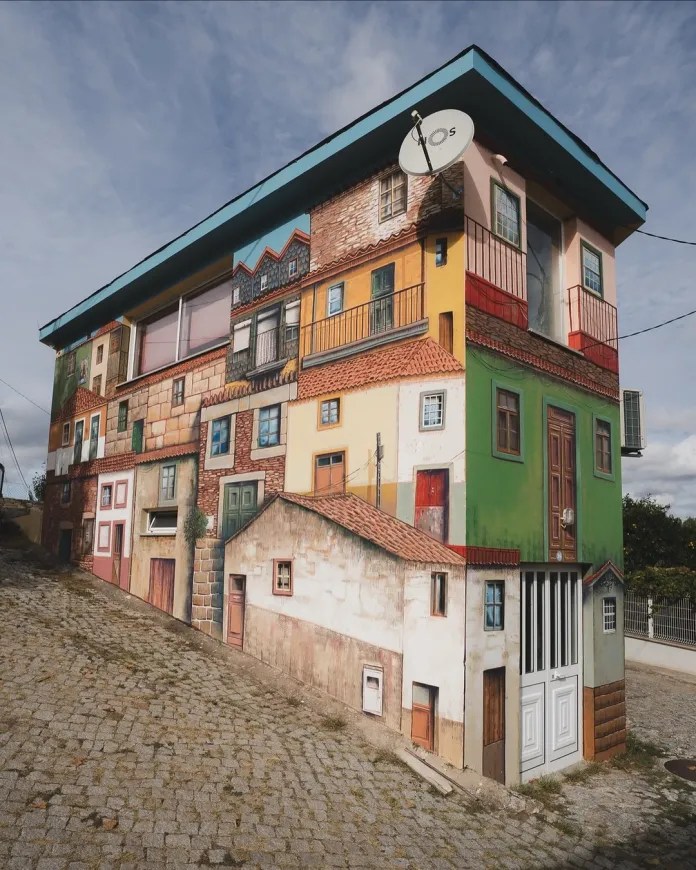 A tall street art mural showing a vertical village of stacked traditional Portuguese houses. Created by street artist Francisco Fonseca in Ôlas, Portugal for the Douro Streetart Festival.