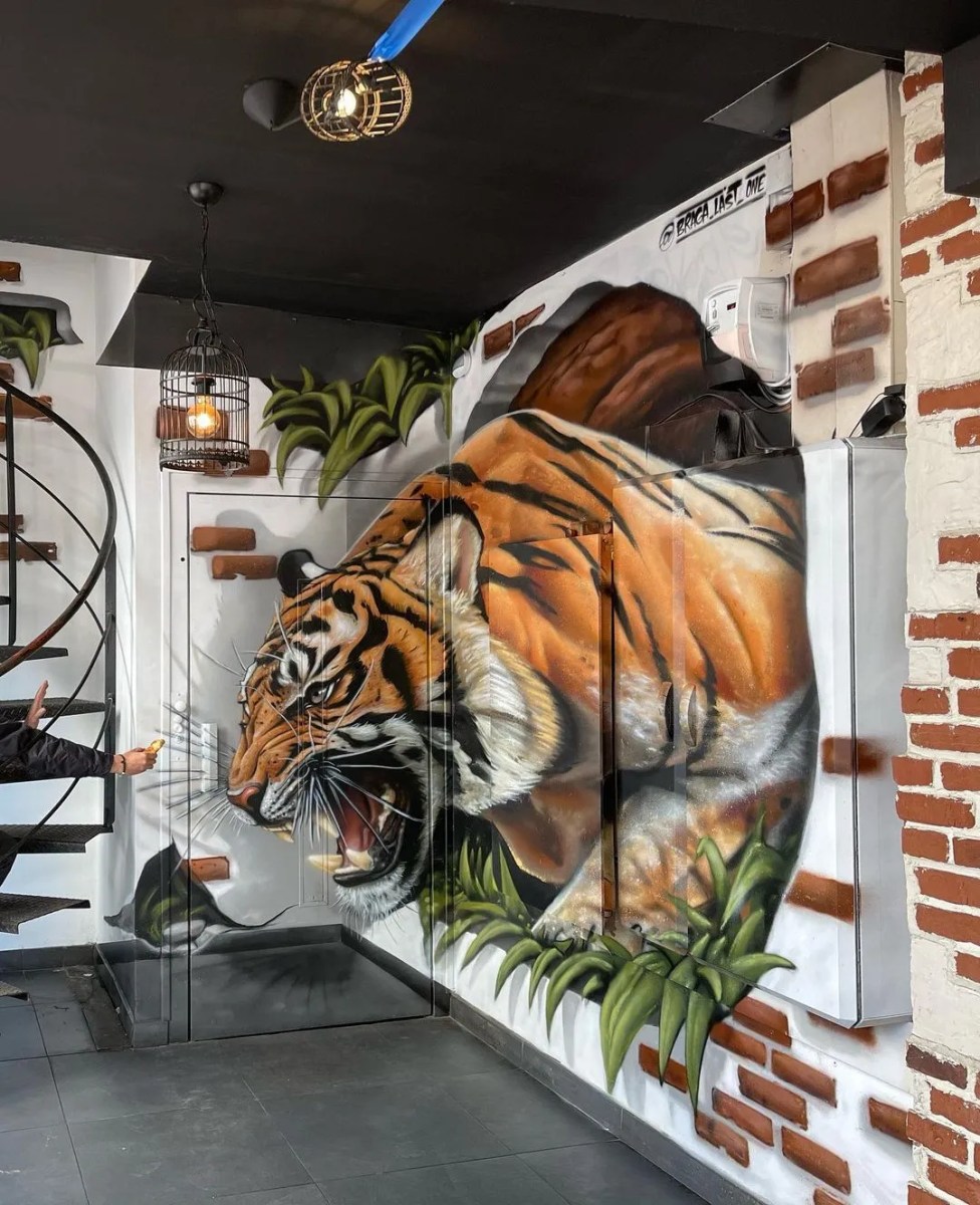 3D painting of a tiger bursting through a brick wall corner with painted flying debris.
