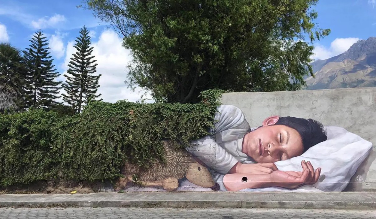 El Decertor's Cobija de plantas mural at Numu Festival in Imbabura, Ecuador, where a living hedge reads as a blanket over a sleeping child.