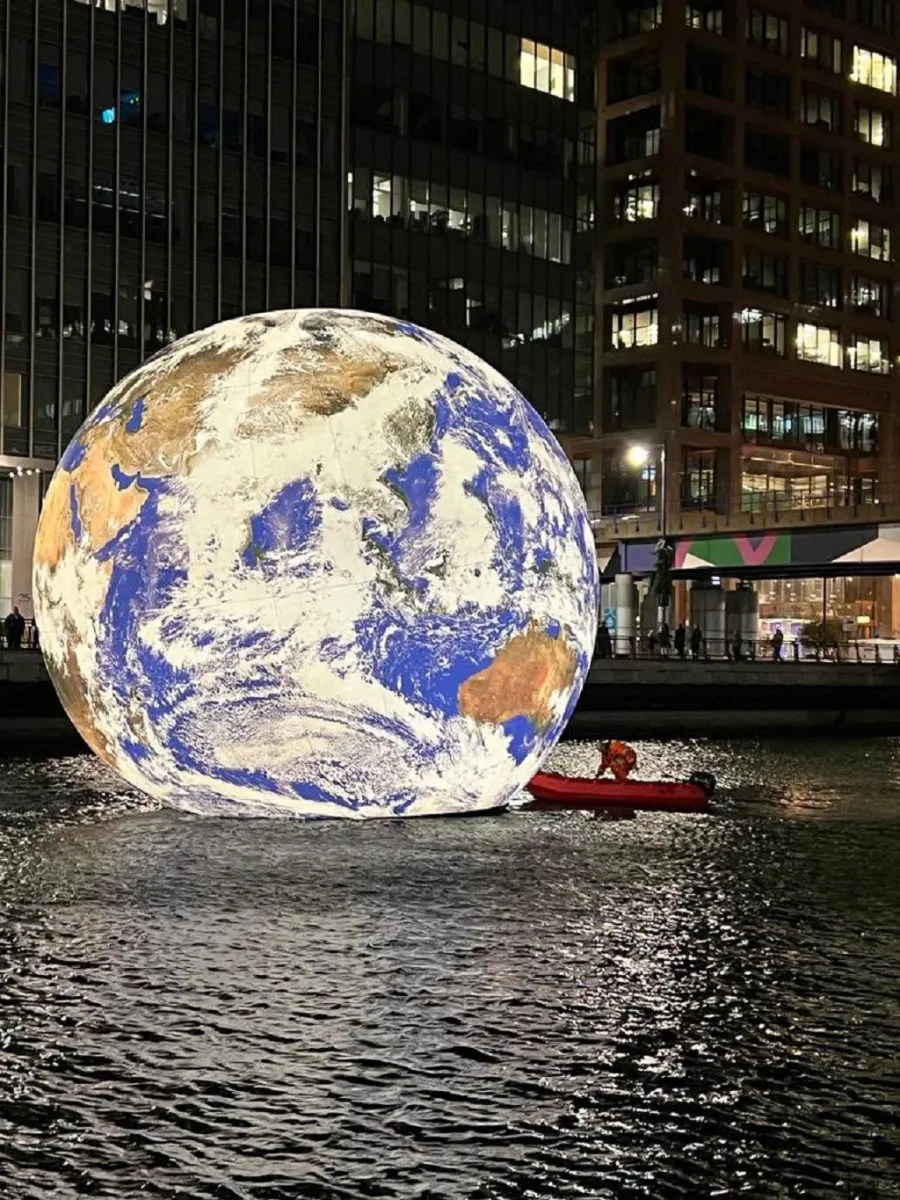 Luke Jerram installation showing a glowing Earth sphere floating on water at night in London.
