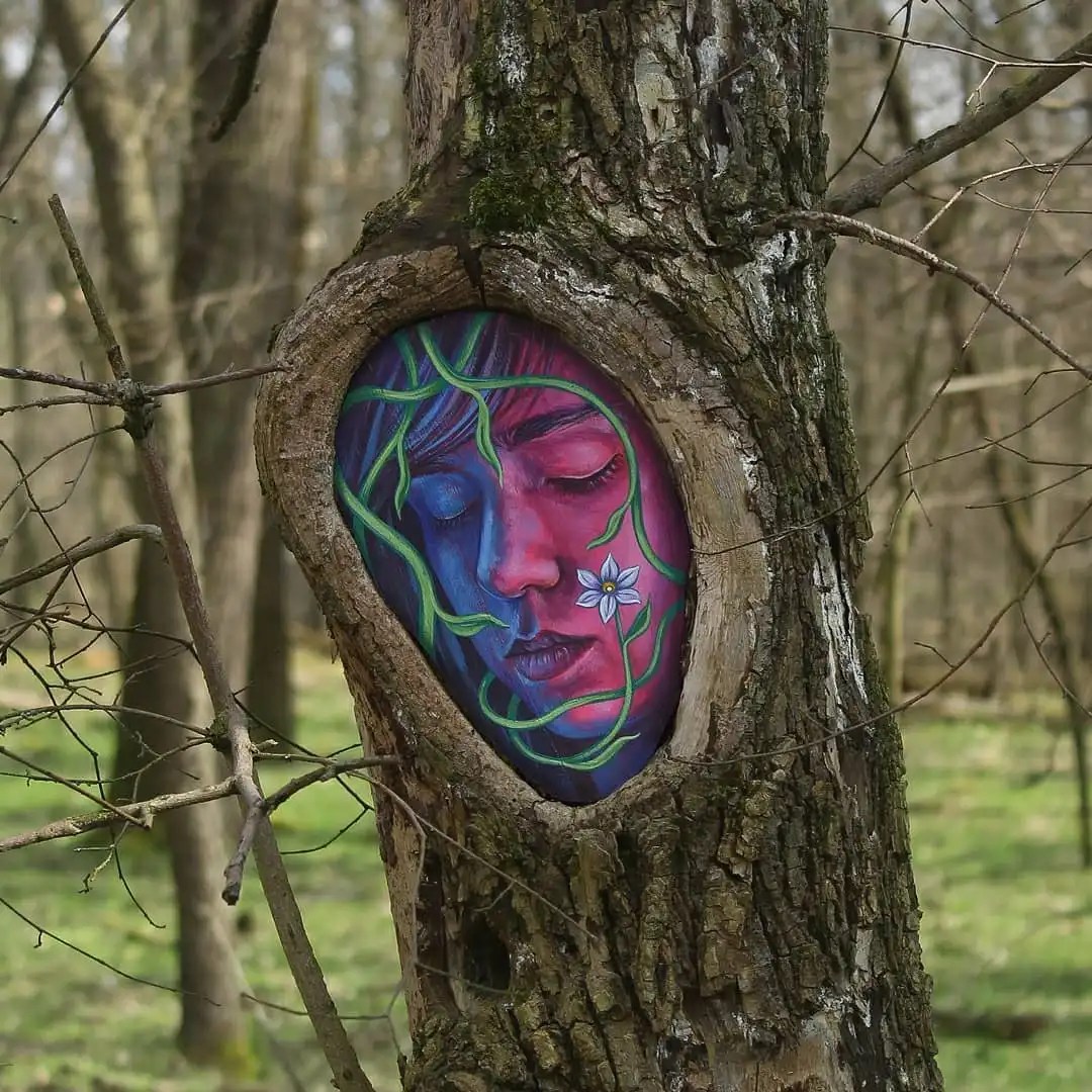 The Trees Also Sleep by Dinho Bento in Nagyerdő, Debrecen, Hungary, showing a sleeping face placed in an exposed patch of a tree trunk in the forest.