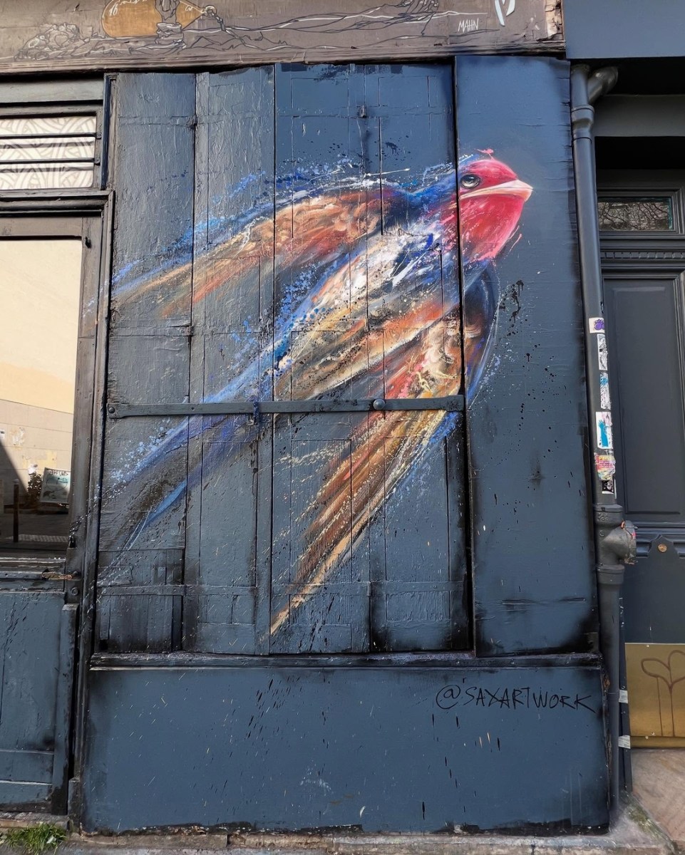 Mural on Paris storefront depicting one dynamic, painterly bird in flight against a deep blue background, with visible motion lines and vibrant feathers.