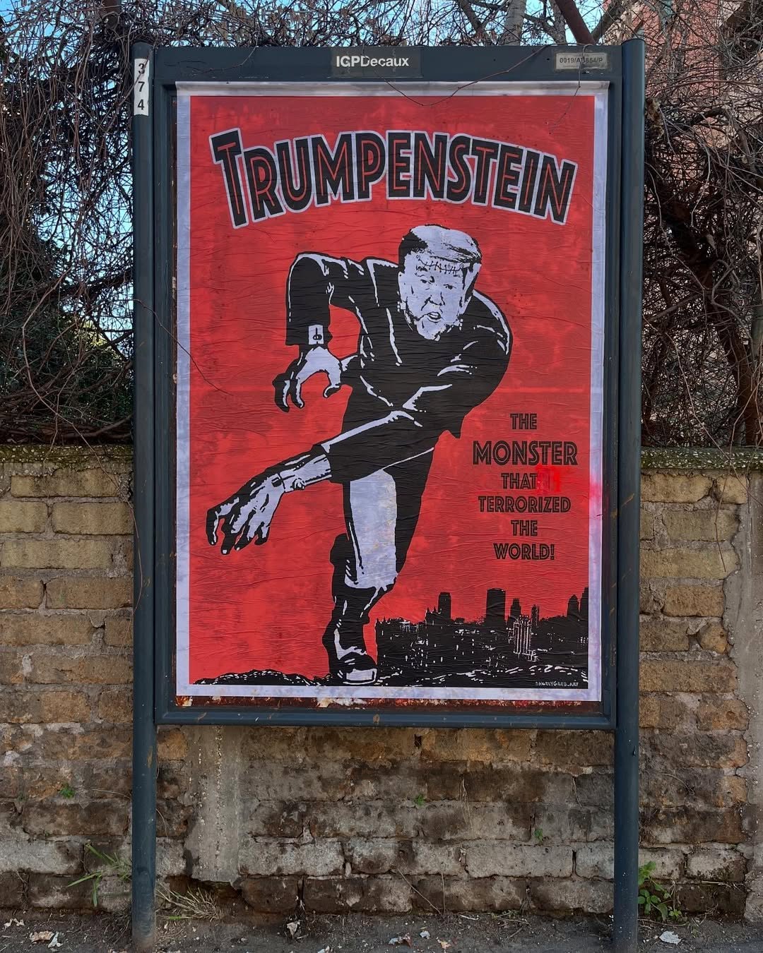 A street art poster by Harry Greb in Rome, Italy, features Donald Trump as Frankenstein’s monster. The artwork mimics a vintage horror movie poster, with a red background, bold black lettering spelling "Trumpenstein," and the tagline: "The Monster That Terrorized The World!" Trump is illustrated in a black suit, hunched over with exaggerated hands reaching forward, with a dark city skyline in the background.