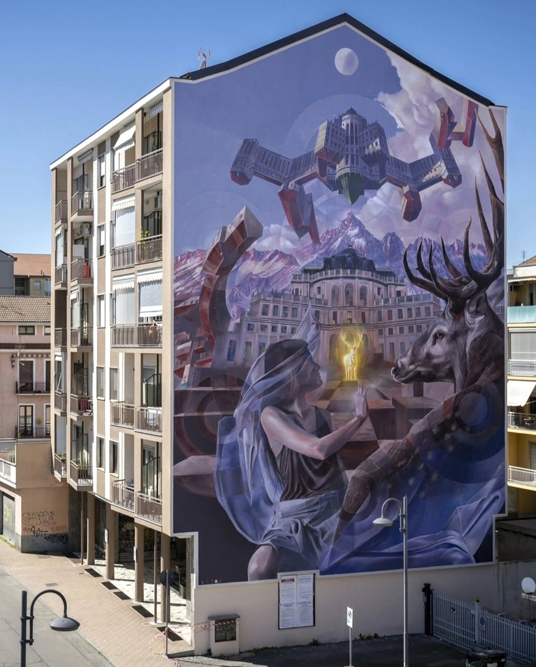 Mural by Vesod in Turin, Italy, showing a veiled woman reaching toward a golden light between her and a stag, with floating buildings and snowy mountains behind her.