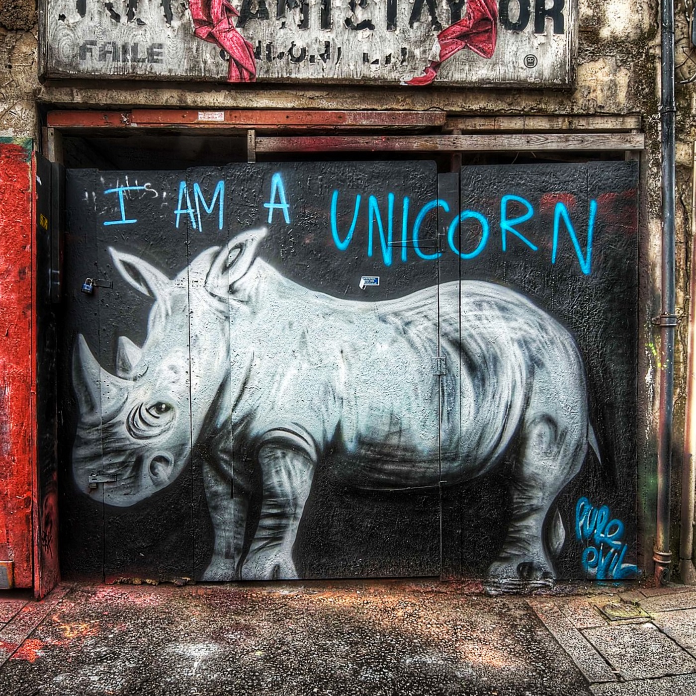 Mural of a gray rhinoceros with “I AM A UNICORN” spray-painted above in bright blue. Painted on a wall in East London by Pure Evil, blending humor with urban grit.