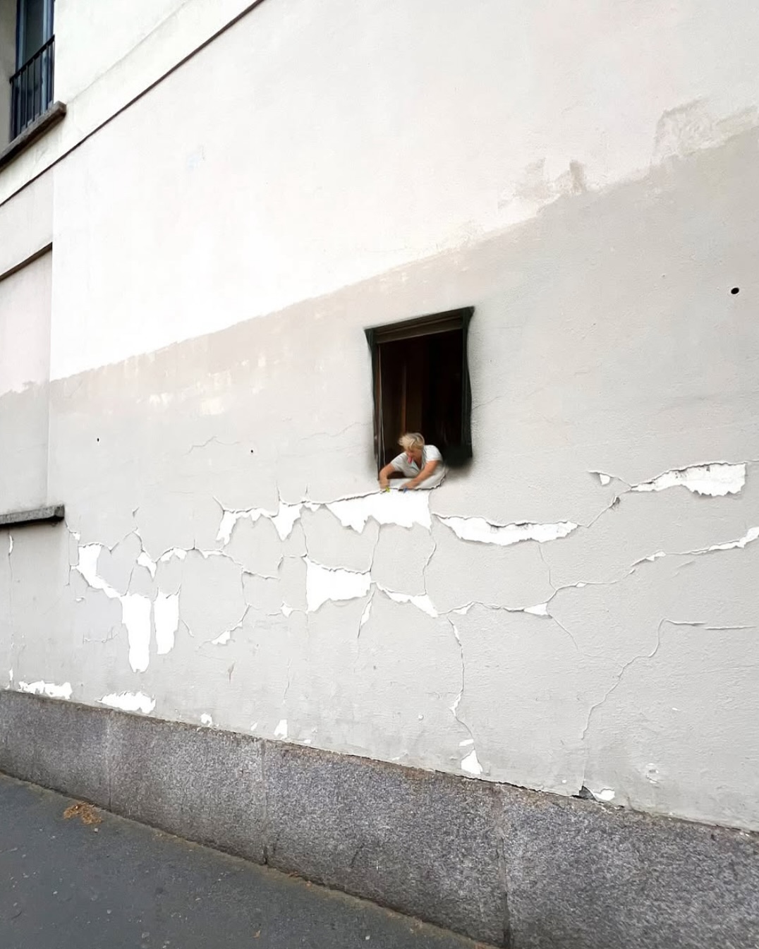 A tiny masterpiece and clever 3D street art by Golsa Golchini in Milan, Italy. A miniature painted woman reaches out of a real wall crevice to hang white laundry on a peeling section of the building.