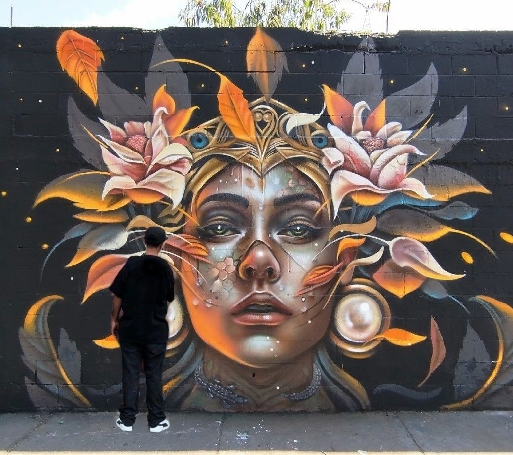 Solvo Ibarra mural in Mexico City of a luminous face framed by petals, feathers, and golden leaves.