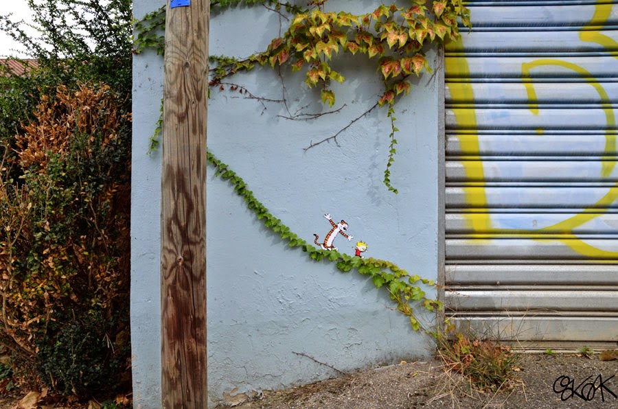 Clever street art by Oakoak featuring Calvin and Hobbes characters sliding down a real wall vine.