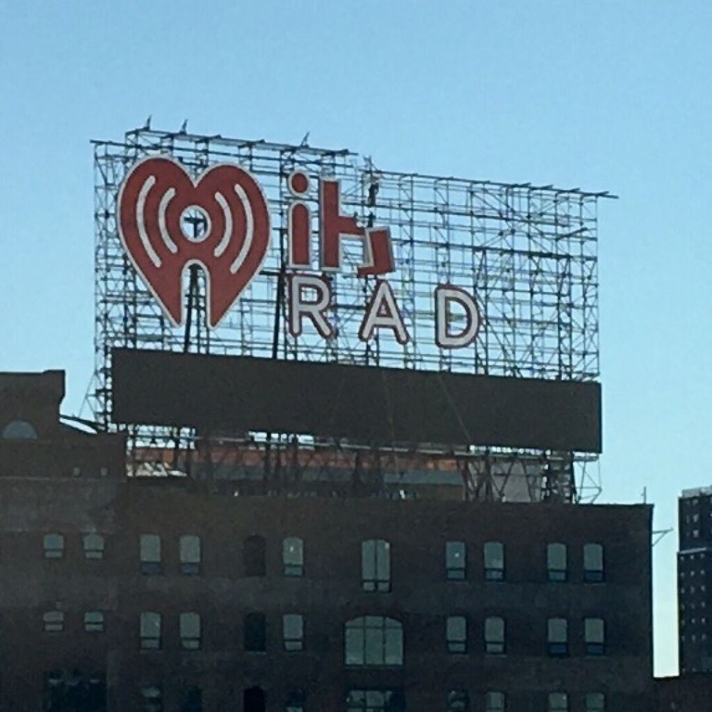 A “I heart Radio” billboard is missing letters on its right-hand half, leaving an “I” and a broken “h” on the top line and the letters “RAD” on the bottom line.