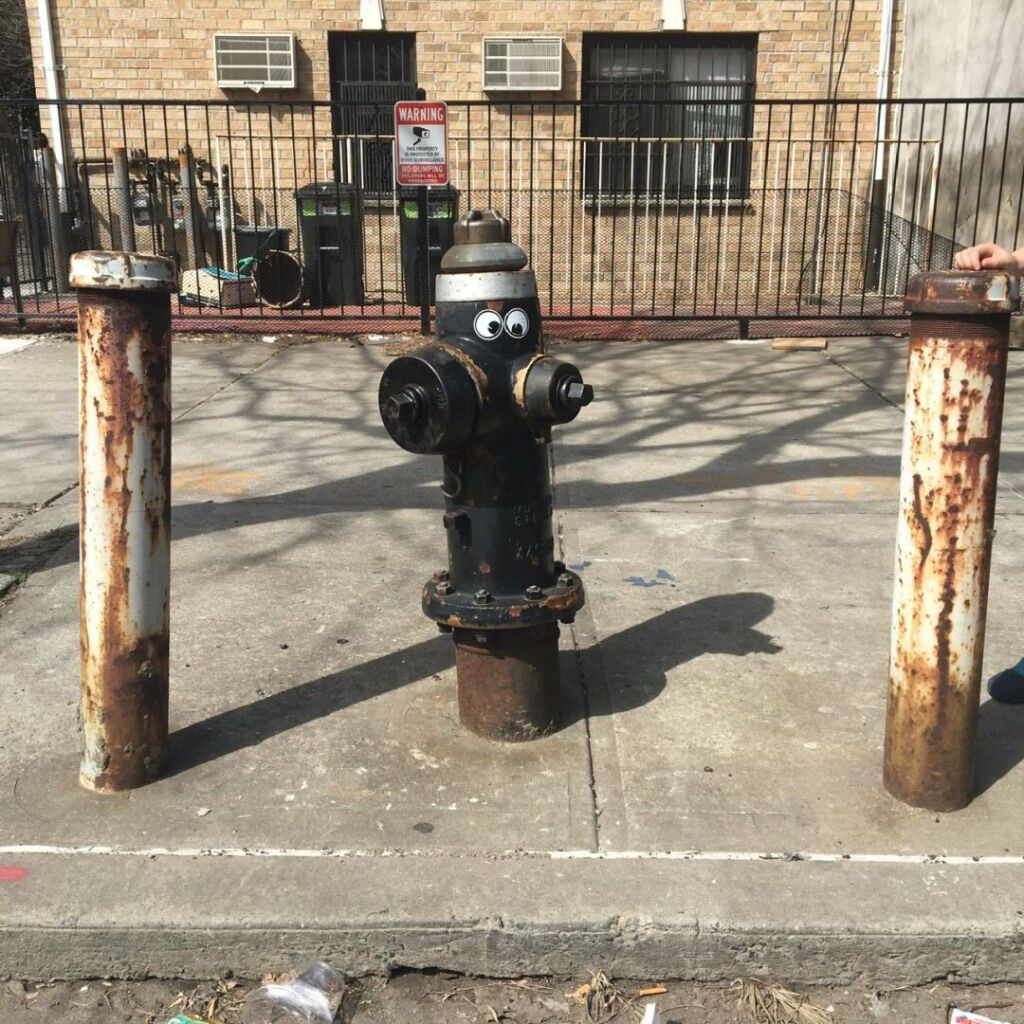 A curbside black fire hydrant is adorned with two large googly eyes looking in different directions.